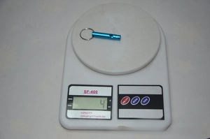 Blue aluminum alloy emergency whistle with key ring being weighed on a digital scale