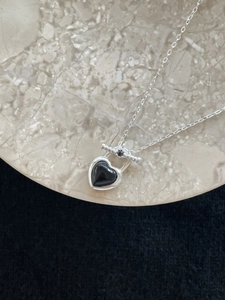 Macro detail of 925 silver necklace featuring black onyx heart pendant on marble
