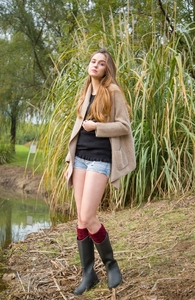 Outdoor view of wine red knit leg warmers styled with matte black rain boots and a long cardigan