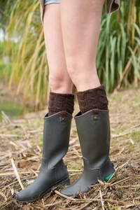 Close-up of cable knit leg warmers in dark brown styled with rubber rain boots in the grass