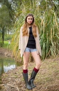 Detail of burgundy cable knit leg warmers worn with tall green rain boots in the nature