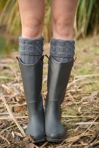 Close-up of gray cable-knit leg warmers with stirrups styled with olive rain boots