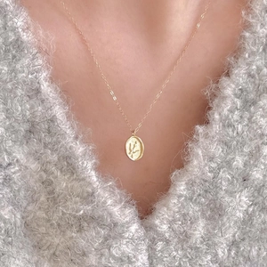 Elegant gold oval pendant necklace with floral relief worn over a grey sweater
