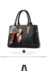Detail of black quilted leather handbag featuring metal logo, pompom charm and floral scarf