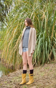 Outdoor lifestyle shot of yellow middle rain boots with knit socks and beige cardigan