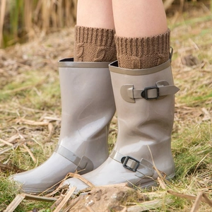 Glossy grey rain boots with brown cable knit leg warmers in an outdoor setting