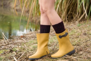 Detail of yellow mid-calf rain boot with side buckle shown in an outdoor grass setting