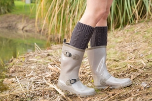 Detail of dark brown cable knit leg warmers paired with glossy grey rain boots
