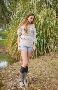Outdoor view of beige cable knit leg warmers paired with grey boots and denim shorts