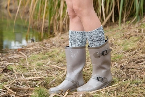 Close-up of glossy rain boots with knit socks and buckle detail in outdoor setting