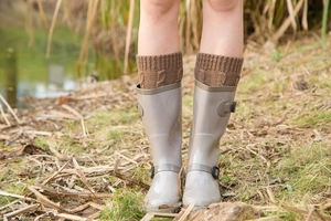 Outdoor detail of brown cable knit leg warmers paired with boots on a grass surface