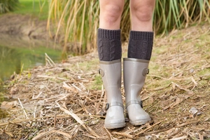 Outdoor close-up of dark grey cable knit leg warmers worn with grey rain boots