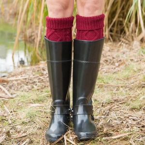 Red cable knit leg warmers for women worn with glossy black boots on grass