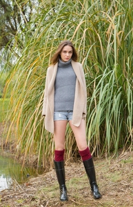 Close-up of red cable-knit over-knee leg warmers paired with black glossy boots in nature
