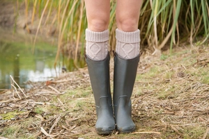 Close-up of thick knitted leg warmers styled with grey rain boots in outdoor reeds