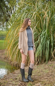 Detailed view of beige knitted leg warmers styled with dark green rubber boots in outdoors