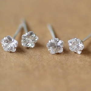 Close-up of four transparent flower shaped stud earrings with silver needles on soft background