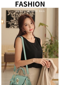 Detail of mint green cross-body bag featuring a pearl handle and floral charm accessory
