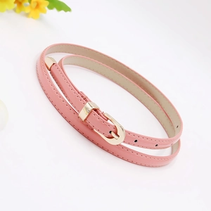 Detail of pink PU leather skinny belt with a gold buckle coiled on a white background