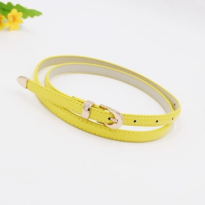 Detail of slim yellow leather belt with gold pin buckle coiled on white background