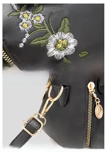 Detailed macro view of daisy floral embroidery and golden metal hardware on black leather bag