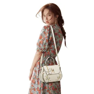 Detail view of white shoulder bag with floral embroidery and golden chain strap on model