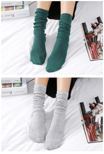 Detailed knit texture of slouch socks in green and light grey shown on a cozy bed