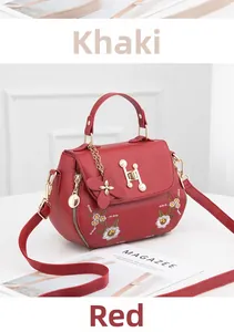 Close-up of red handbag featuring intricate white floral embroidery and floral pendant