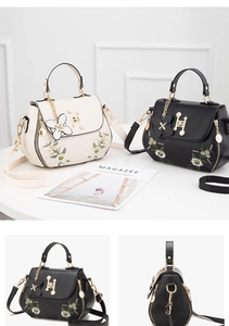 Close-up of floral embroidery detail and elegant metal H-clasp on black leather handbag