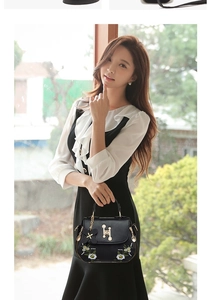 Detail of floral embroidery and pearl H-buckle on a black leather crossbody handbag