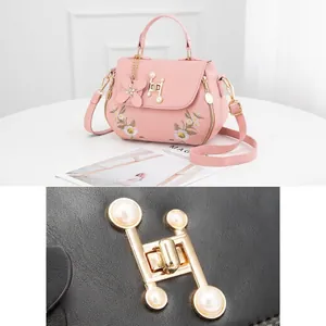Detailed macro of H-shaped gold buckle with pearls and floral embroidery on pink bag