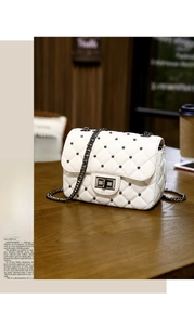 Detailed shot of white quilted chain bag with metal studs and twist lock on wooden desk