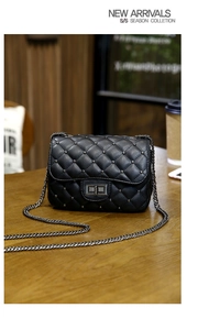 Detail of black quilted leather crossbody bag with silver studs on a wooden table