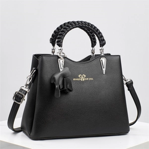 Black lychee leather handbag with woven handle and adjustable strap in studio
