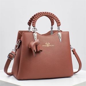 Detail view of caramel brown lychee leather handbag with woven handles and gold logo