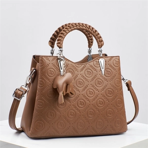 Detalle de bolso de cuero marrón con patrón LD en relieve, asa trenzada y un colgante