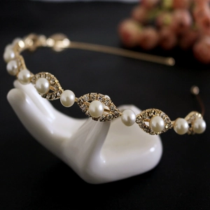 Detail shot of a gold pearl headband with sparkling rhinestones on a white mannequin hand