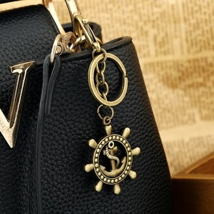 Vintage bronze anchor and helm keychain pendant displayed on a premium leather bag