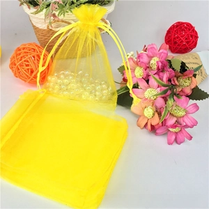 Detail view of yellow organza drawstring gift bag with pearls on light background