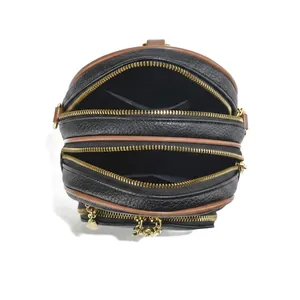 Detail van zwarte crossbodytas van generfd leer met meerdere ritsvakken en goudkleurige hardware