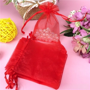 Detail of red organza drawstring bags with shimmering beads inside on pink backdrop