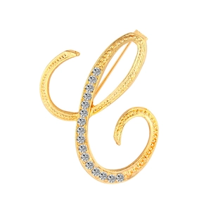 Macro detail of golden letter C brooch featuring twisted metal texture and inlaid rhinestones