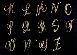 Collection of gold letter brooches with sparkling diamonds from K to Z on black backdrop