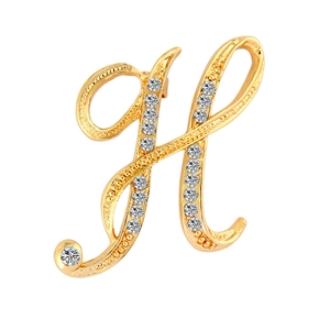 Macro detail of gold-plated H-letter brooch with sparkling inlaid crystals on white background