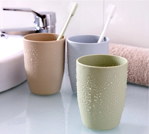Close-up of minimalist plastic mouthwash cups in beige, blue, and green on bathroom counter