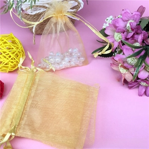 Close-up of golden organza drawstring gift bag with pearls on pink background