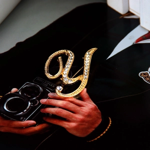 Golden letter Y brooch with sparkling rhinestones pinned on dark fabric with a vintage camera