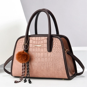 Rosa Handtasche mit Krokodilmuster, dunkelbraunen Griffen und flauschigem Pompon