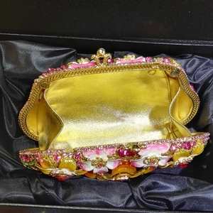 Detail of gold metal evening clutch showing floral enamel work and rhinestones in gift box