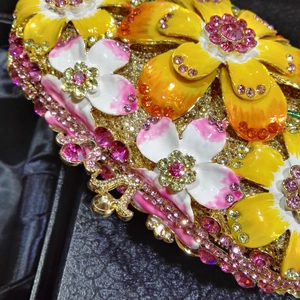 Close-up of golden evening clutch featuring floral enamel and sparkling pink rhinestones